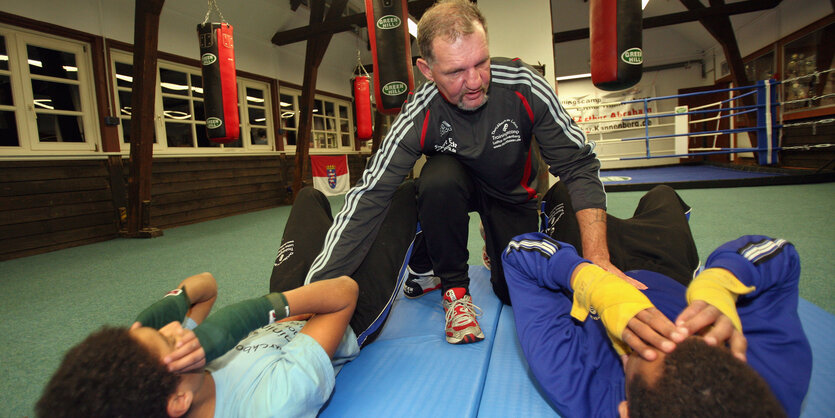 Lothar Kannenberg drückt zwei Jungen auf eine Turnmatte.