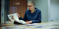Frau mit grauem Haar und Brille blättert in dickem Buch mit bunten Bildern