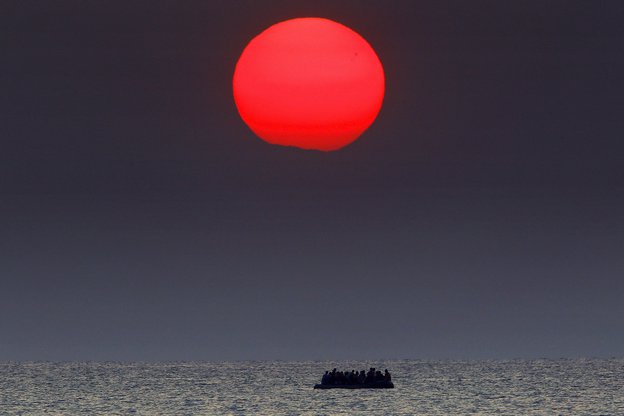 Ein Flüchtlingsboot treibt unter einer großen, roten Sonne dahin