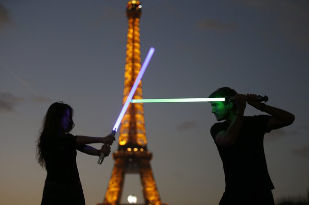 Zwei Menschen kämpfen mit Laserschwertern vor dem erleuchteten Eiffelturm