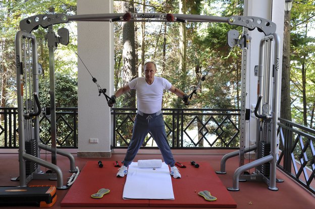 Wladimir Putin steht unter einem Fitnessgerät mit ausgebreiteten Armen