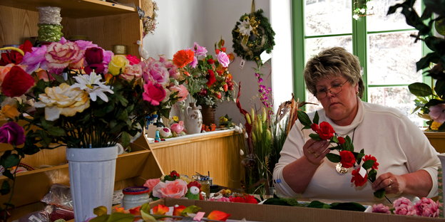 Eine Frau fertigt Kunstblumen, neben sich ein großer, bunter Straus in einem Eimer