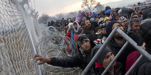 Viele Menschen warten an einem Grenzzaun.