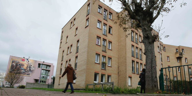 Eine Frau läuft vor einem beige-grauen Wohnblock vorbei