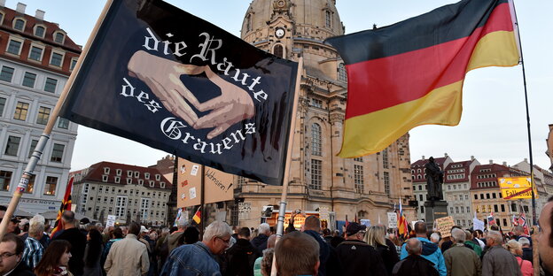 Pegida-Anhänger vor der Frauenkirche mit Deutschlandfahne und einem Transparent auf dem „die Raute des Grauens“ steht