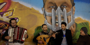Menschen machen Musik vor einem Grafitti, das einen Mann mit Maulkorb zeigt