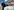 Ein Mann mit Trump-Maske reitet auf einer Atombombenattrappe, im Hintergrund Menschen mit Schildern „STOP The Arms Race!“ vorm Brandenburger Tor