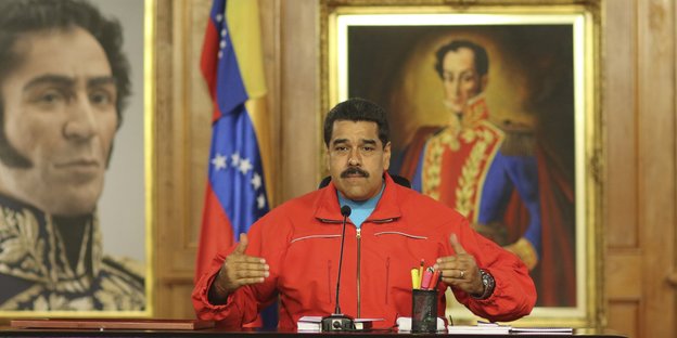 Nicola Maduro steht vor Ölgemälden und hebt die Arme