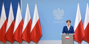 Beata Szydlo gibt eine Pressekonferenz, nur mit polnischen Flaggen im Hintergrund