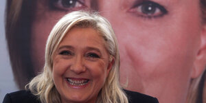 Marine Le Pen sitzt lächelnd vor einem großen Foto von ihr selbst