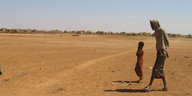 Ein Mann und ein Kind gehen über eine trockenes Feld.