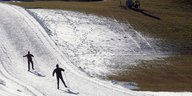 Zwei Skifahrer fahren eine Kunstschnee-Piste hinauf