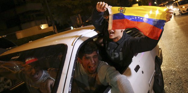 Männer im Auto schwenken die venezolanische Flagge.