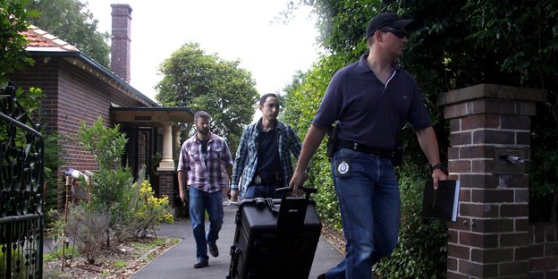 Australische Zivilpolizisten laufen eine Auffahrt entlang, einer hat einen Rollkoffer