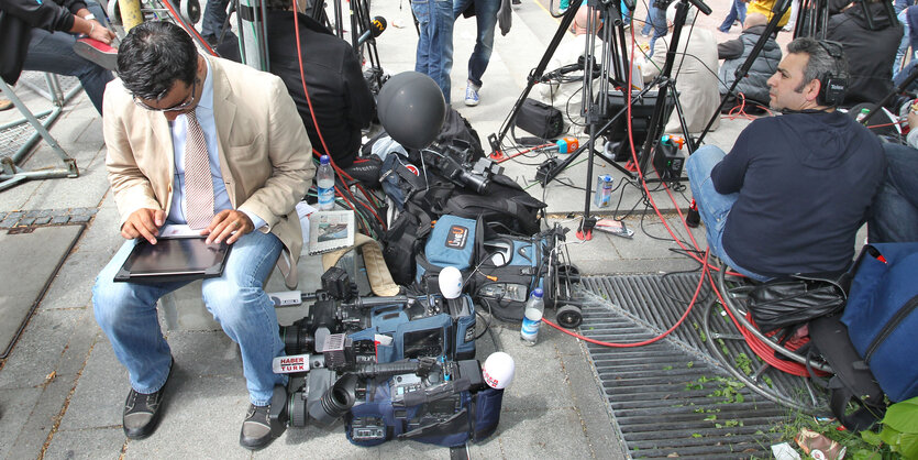 Ein Mann mit einem Tabletcomputer sitzt neben Fernsehkameras