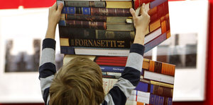 Eine Junge balanciert viele Bücher auf einmal.