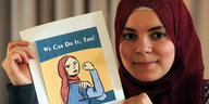 Eine Frau mit Kopftuch hält eine Comiczeichnung hoch, auf der eine Frau ihre Muskeln zeigt