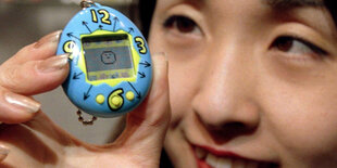 Eine Frau hält ein Tamagotchi hoch