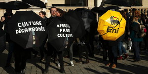 Klimaaktivist_innen halten schwarze Regenschirme mit Parlen gegen die Nutzung fossiler Brennstoffe hoch