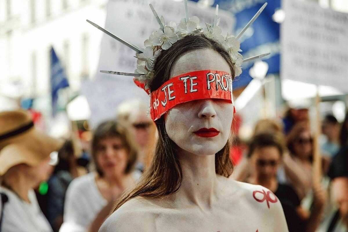 Eine Frau ist verkleidet, sie hat sich geschminkt und trägt eine rote Binde über ihren Augen. So protestiert sie mit anderen