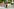 Ein Bauarbeiter in orangener Weste steht auf einer Baustelle und hält einen Sonnenschirm