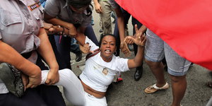 Eine Frau in weißer Kleidung wird an Armen und Beinen festgehalten