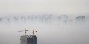 Ein Hochhaus wird gebaut, die Luft voll Smog, eine Skyline schimmert durch