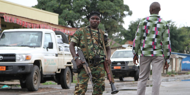 Ein bewaffneter Soldat steht in Bujumbura/Burundi auf der Straße. Neben ihm, ein Passant.