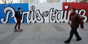 Passanten laufen und skaten vor einer in Nationalfarben und mit „Paris je t'aime“-bemalten Wand