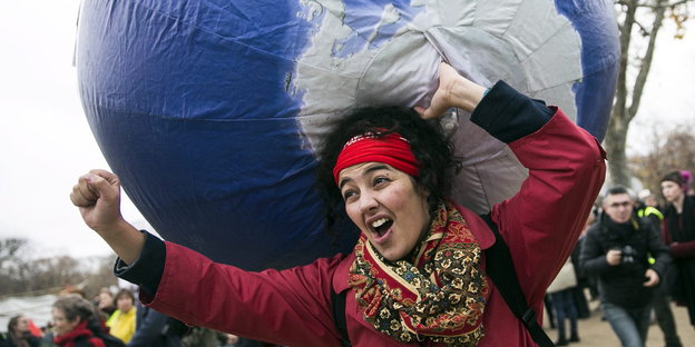 Eine Frau trägt einen Globus und reckt die Faust in die Höhe.