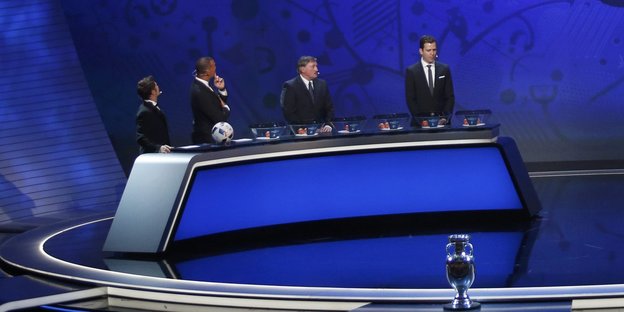 Männer in Anzügen stehen bei der Auslosung zur Fußball-EM 2016 vor Lostöpfen