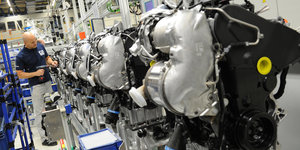 Mehrere Motoren in einer VW-Fabrik, im Hintergrund ein Monteur