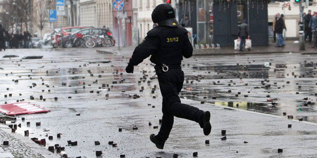 Ein Polizist in voller Kampfmonitur auf einer von Pflastersteinen übersäten Straße