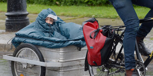 Ein Kind im Regencape sitzt in einem Rad-Anhänger