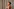 Ariana Grande steht im schulterfreien Kleid vor einem Vorhang und dreht sich winkend um