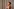 Ariana Grande steht im schulterfreien Kleid vor einem Vorhang und dreht sich winkend um