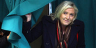 Marine Le Pen schaut hinter dem Vorhang einer Wahlkabine hervor.