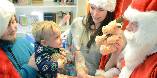junge Eltern mit Kind, das vom Weihnachtsmann beschenkt wird