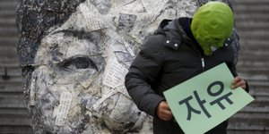 Ein Mensch trägt eine Maske und Protestschilder