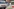 Absperrgitter vor einem Polizeiauto und Polizisten in weißen Schutzanzügen