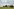 Alleinstehendes Haus in der Landschaft, Bäume im Garten und auf dem Feld - eine Stromtrasse und Windkraftwerke im Hintergrund