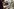 Eine Frau mit Brille sitzt in einer Textilfabrik und arbeitet an einem gestreiften Kleidungsstück