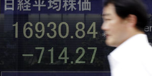 Mann vor einer Börsenkurstafel mit fallenden Kursen