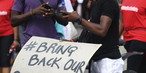 Zwei Nigerianer an ihren Mobilfunkgeräten über einem Kampagnenschild