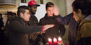 Vier Flüchtlinge in einer Kirche, sie wärmen ihre Hände über den Kerzen auf einem Adventskranz