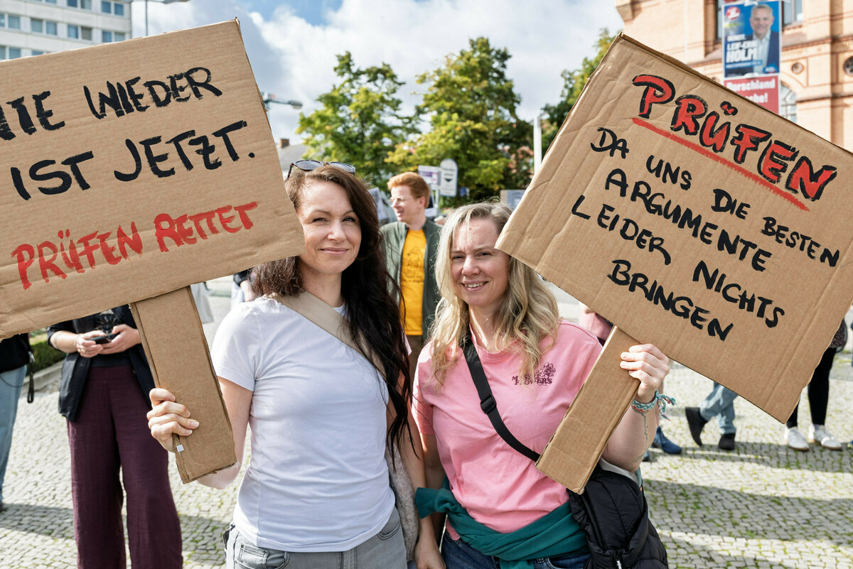 Zwei Frauen halten während einer Demonstration Schilder mit den Aufschriften "Nie wieder ist jetzt. - Prüfen rettet."