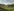 Blick in eine hügelige Landschaft mit grünem Gras überzogen und Strommasten im Gelände