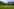 Eine Blumenwiese, im Hintergrund grüne Gebirgsketten und Wolken am Himmel