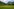 Eine Blumenwiese, im Hintergrund grüne Gebirgsketten und Wolken am Himmel