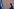 Die Richterin Tomoko Akane geht in einer blauen Robe an einer Wand entlang, links in der Ecke die blaue Flagge des Internationalen Strafgerichtshofs